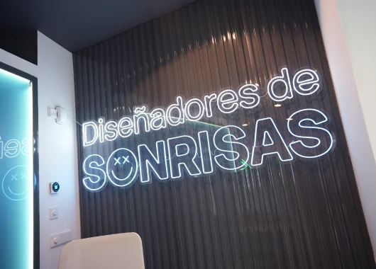 A modern interior featuring a wall with the neon sign "Diseñadores de SONRISAS" against a textured background.